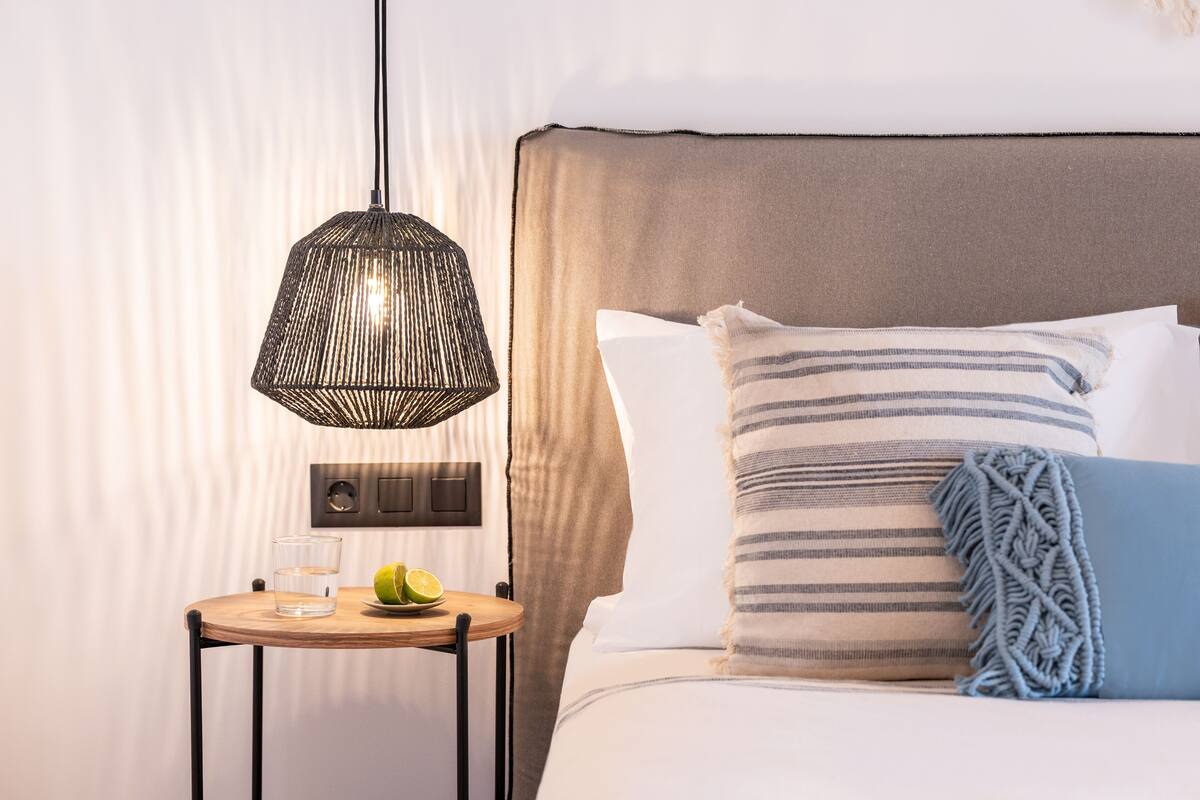 A neatly arranged hotel room with a bed, a bedside table with a glass of water and a lime, and a hanging light fixture.