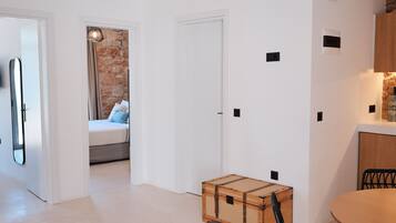 Una habitación moderna y luminosa con una mesa de madera, una taza azul, una silla negra, una maleta y una cama con pared de piedra y cortinas.