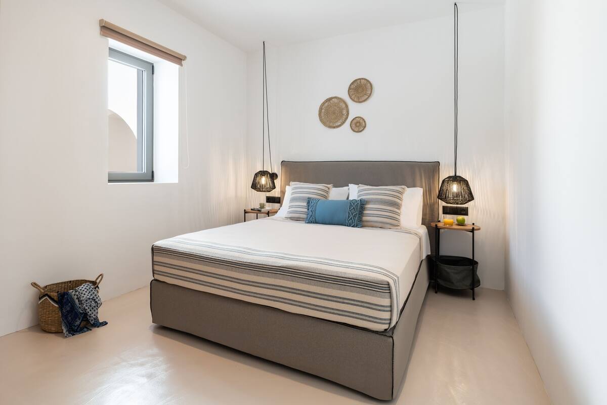 A modern bedroom with a large bed, two bedside tables, a small window, and decorative wall art.