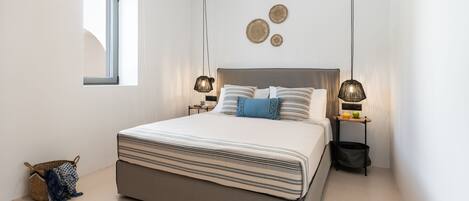 Un dormitorio moderno con una cama grande, dos mesitas de noche, un ventanal pequeño y decoración en la pared.