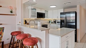 A modern kitchen with white cabinets, a black refrigerator, a microwave, and a bar area with stools.