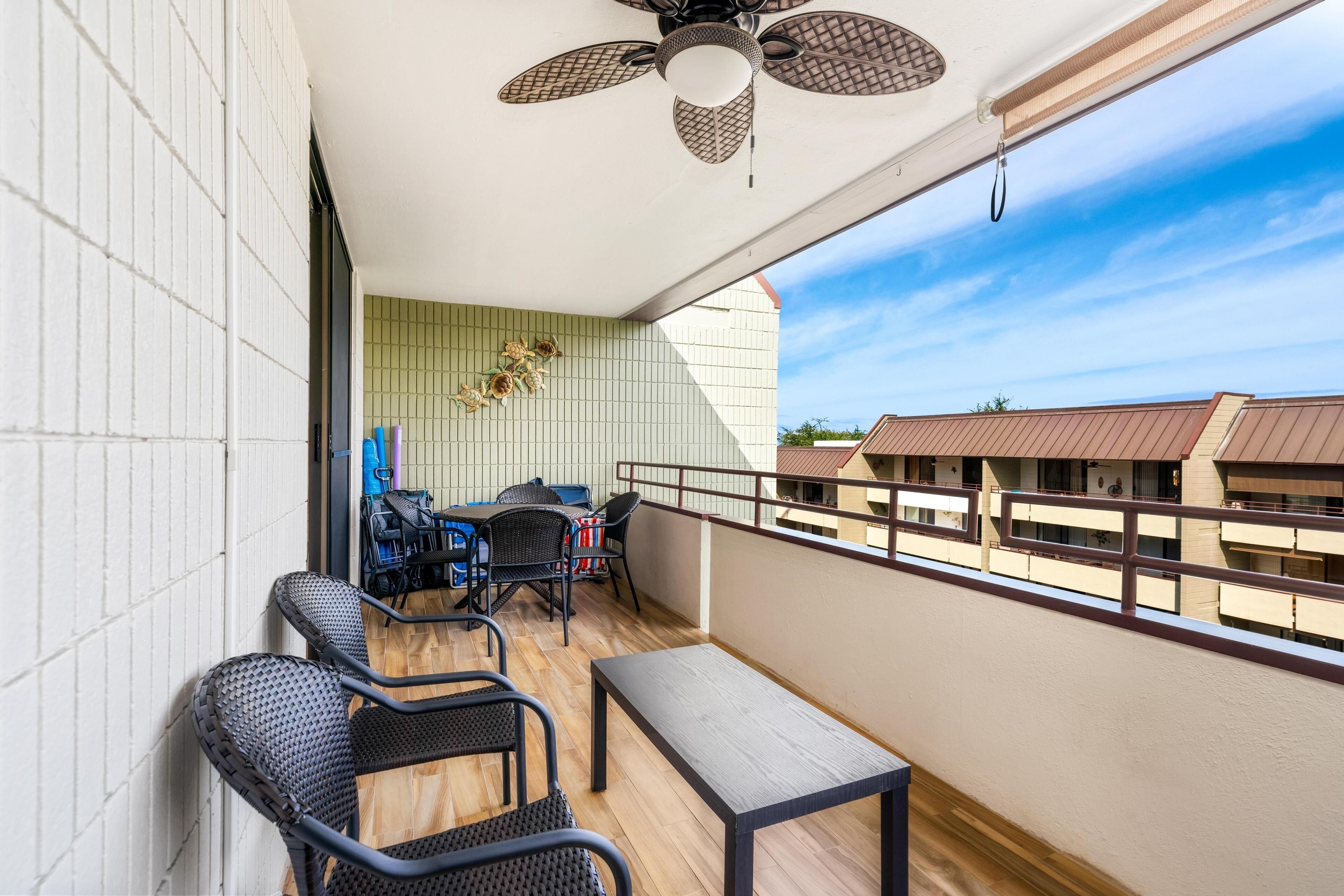 A balcony with wicker chairs, a table, and a ceiling fan.