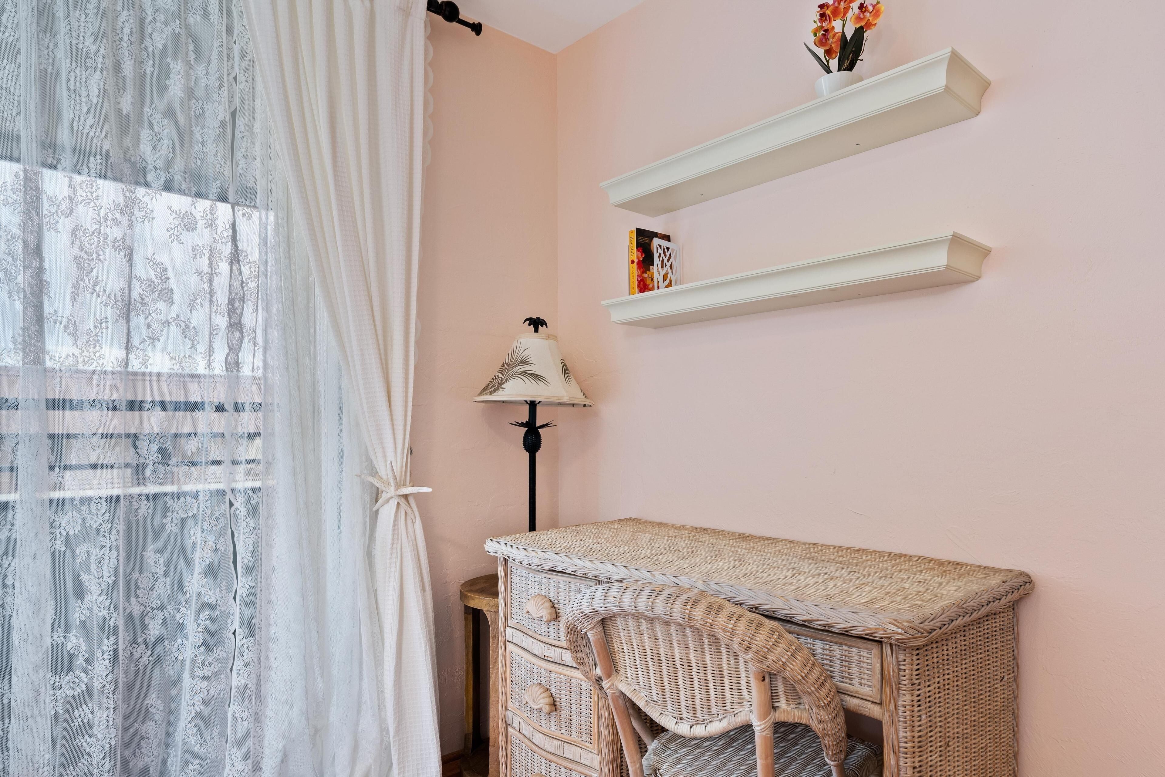 Ein Zimmer mit einem Korbmöbel-Schreibtisch, einer Lampe und zwei weißen Regalen.