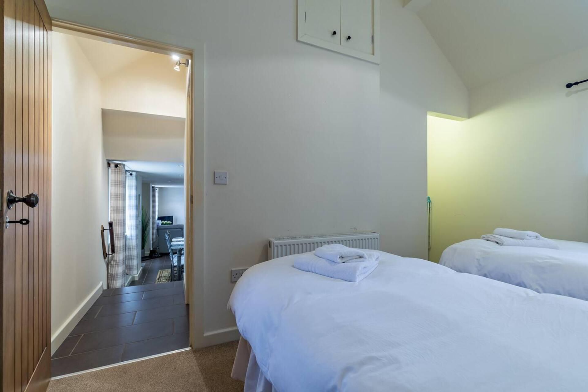 A hotel room with two beds, a radiator, and a wooden door leading to a hallway.