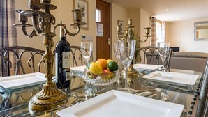 Una mesa de comedor dispuesta con una botella de vino, fruta y copas, rodeada de candelabros ornamentales.