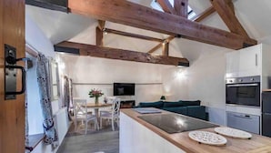 A modern kitchen with wooden beams, a dining area with a table and chairs, and a sofa in the background.