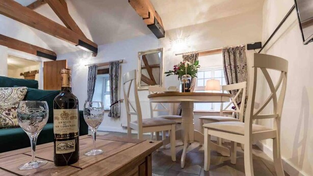 A cozy room with a wooden table, two wine glasses, and a bottle of wine. There is a green sofa and a white dining table with chairs.