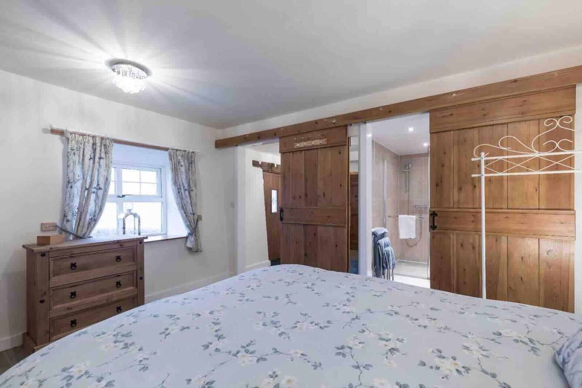 A bedroom with a large bed, wooden wardrobe, and a window with curtains.