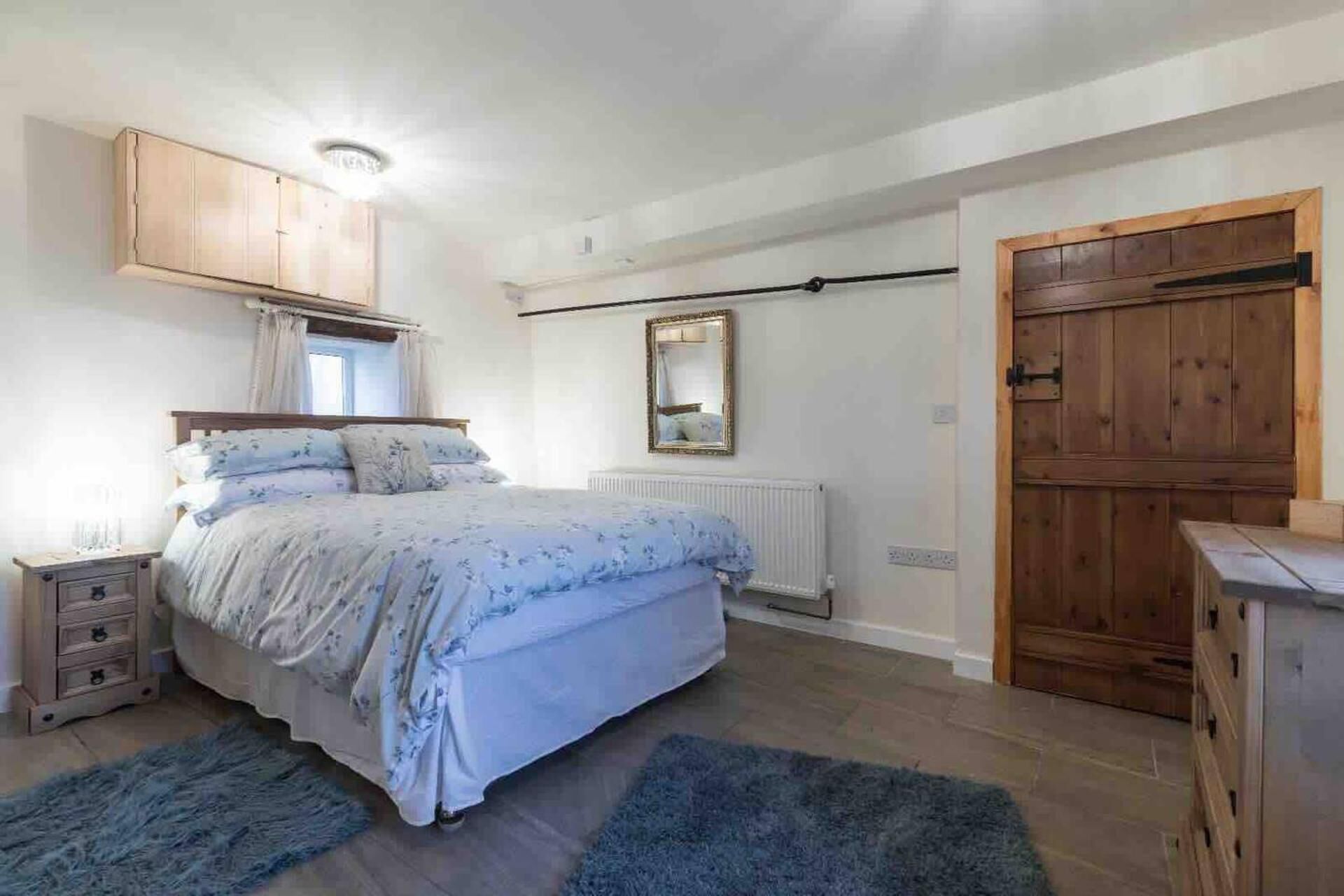A bedroom with a bed, wooden wardrobe, a mirror, and a radiator.