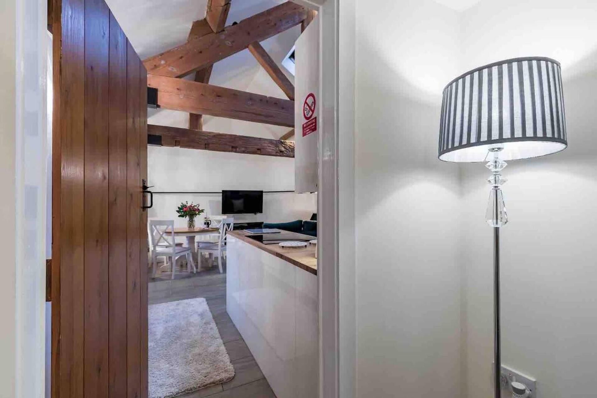 A modern kitchen with wooden beams, a dining area with chairs and a table, and a floor lamp.