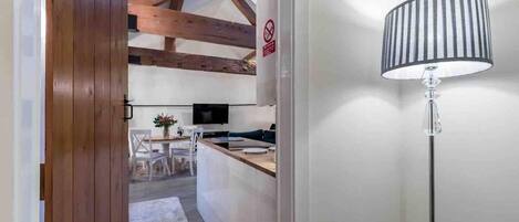 Una cocina moderna con vigas de madera, una zona de comedor con sillas y una mesa, y una lámpara de pie.