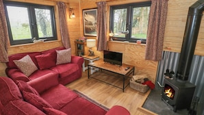 Un interior de cabaña acogedor, con un sofá rojo, televisor, chimenea y ventanas amplias.