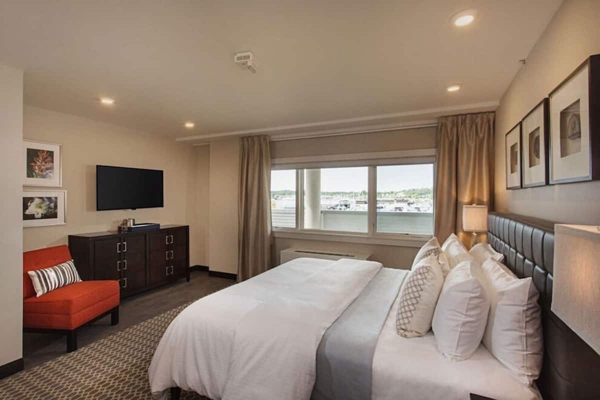 A hotel room with a large bed, a TV, a red sofa, and a window with a view of a body of water.