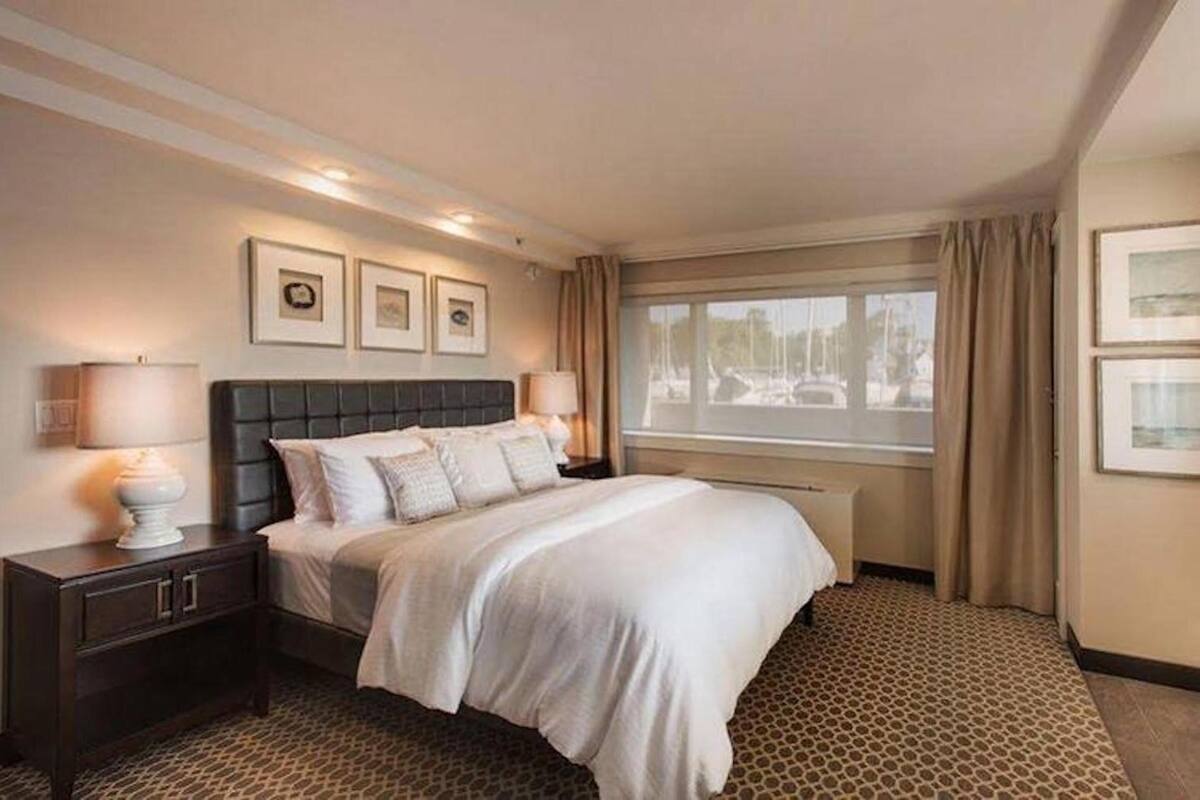 A hotel room with a large bed, a nightstand, a window with curtains, and framed pictures on the wall.