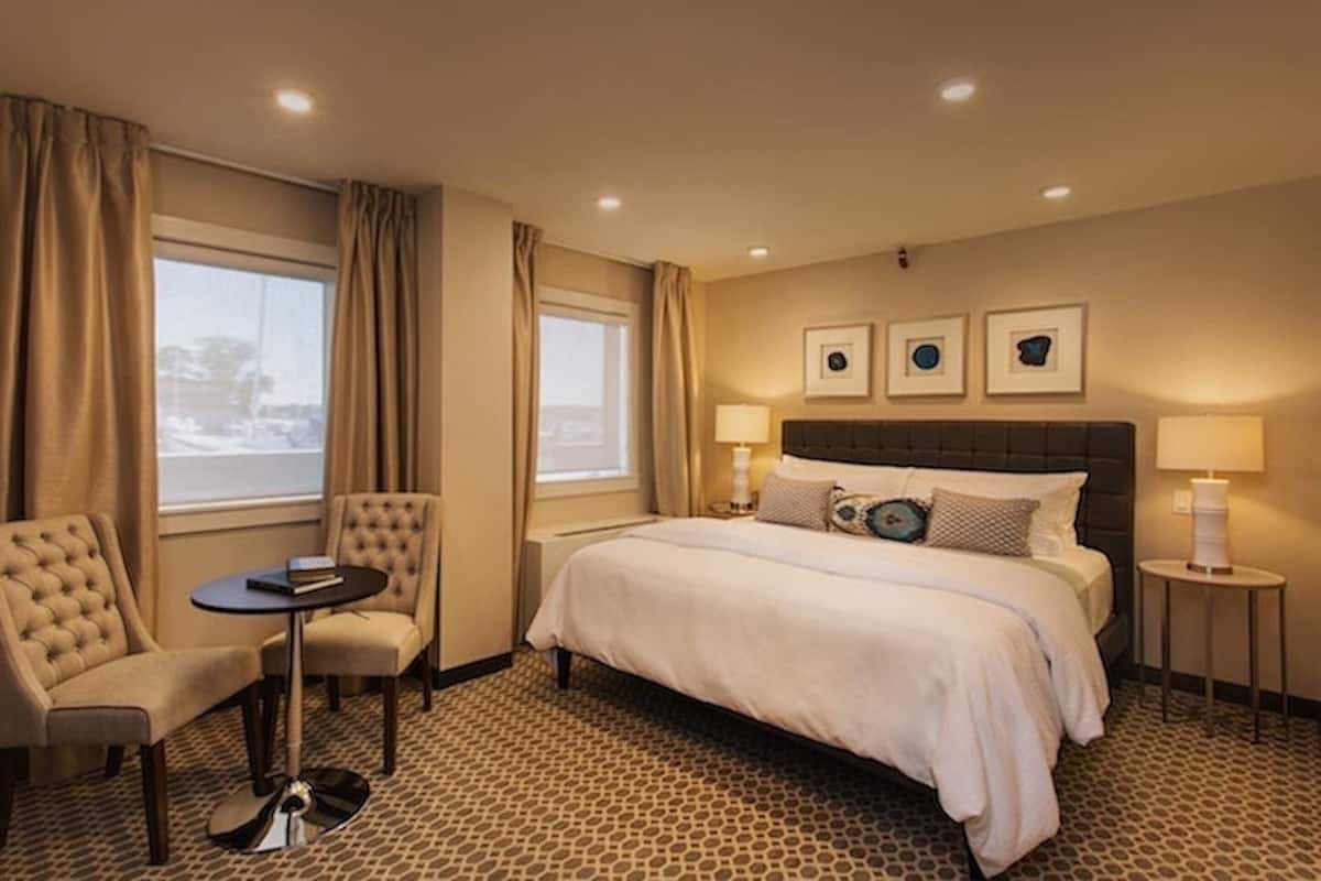 A hotel room with a large bed, two armchairs, a small table, and two bedside lamps. There are three framed pictures on the wall above the bed.