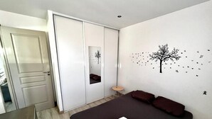 A bedroom with a bed, a wardrobe, a mirror, and a wall decoration. - Cosy apartment, 100 m from beaches, quiet area with outside, air conditioning, wifi & parking (Saint-Chamas)