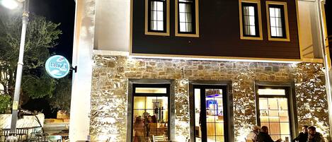 A building with a stone facade, multiple windows, and outdoor seating area with tables and chairs.