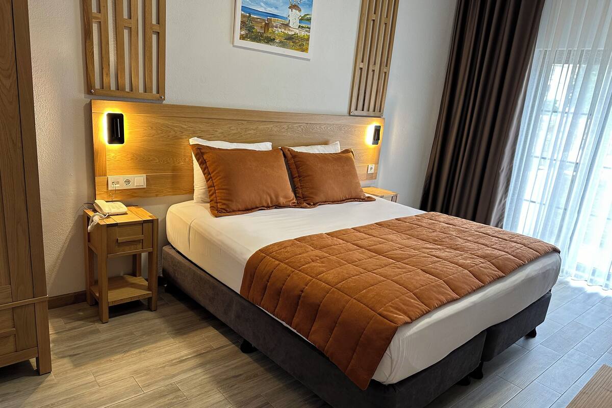 A hotel room with a large bed, wooden headboard, bedside tables, and a painting on the wall.