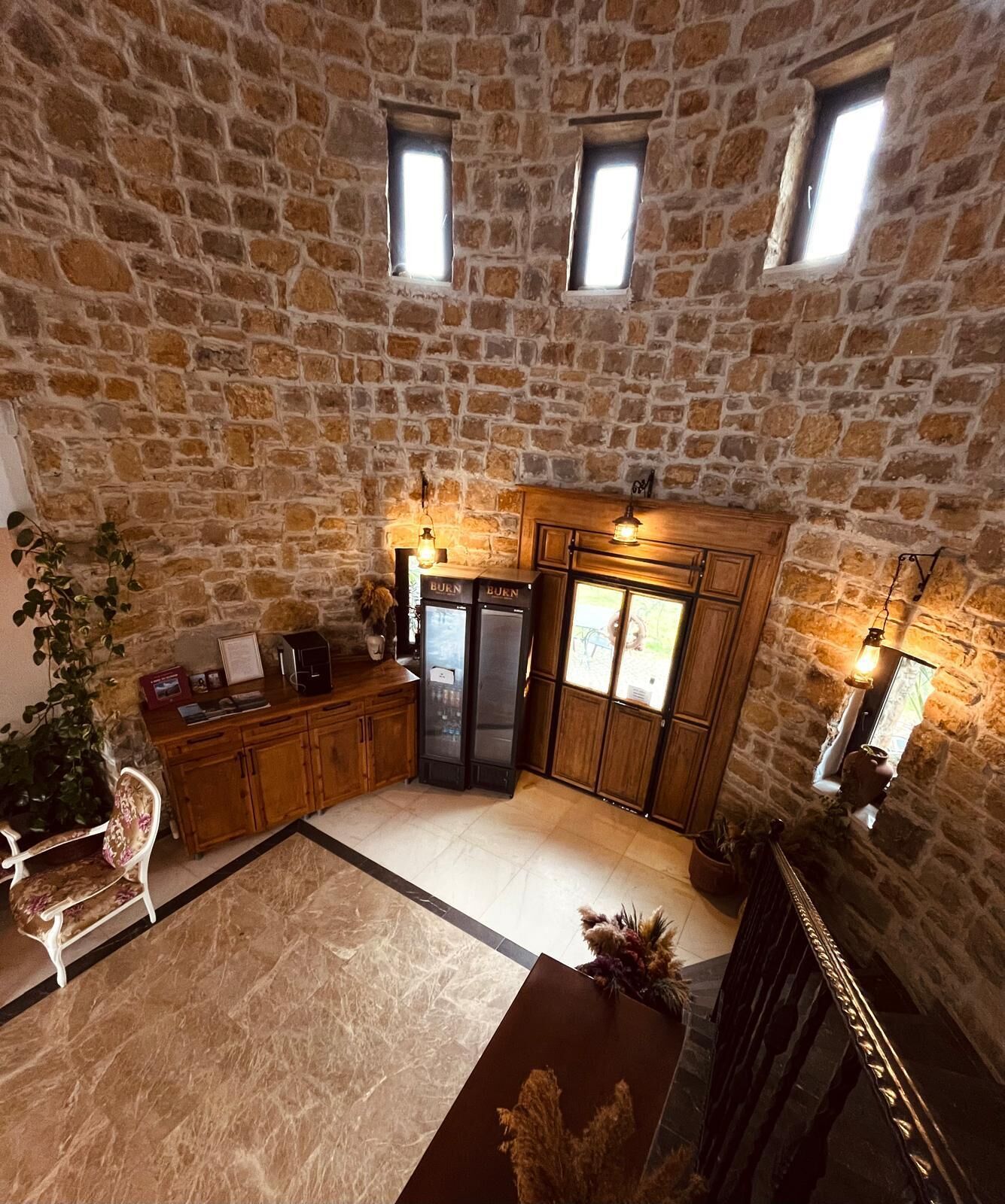 A stone-walled kitchen with built-in cabinets, a refrigerator, and a dining area with a chair and table.