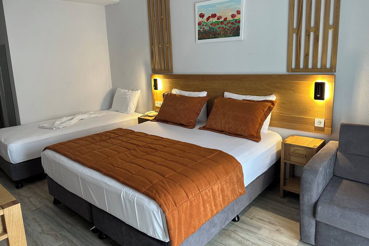 A hotel room with two beds, a wooden headboard, bedside lamps, a painting, and a gray armchair.
