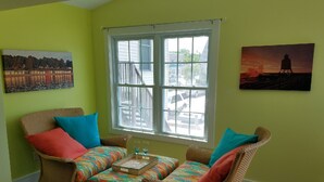 Una habitación con dos sillones de mimbre, una mesita y un ventanal con vistas a la calle y edificios.