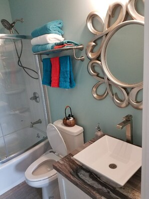 A bathroom with a shower, toilet, and sink. There are towels on a rack and a decorative mirror. - Artsy Downtown Charlevoix apt! Walk  to 2 lakes, marina. Free Parking. 5 star (Charlevoix)