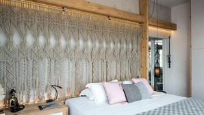 Une chambre à coucher avec une tête de lit en macramé, un lit recouvert de plusieurs coussins, une table de chevet avec une lampe et une petite statue de Bouddha.