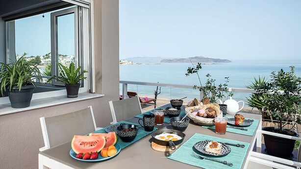 Une table sur le balcon, avec des éléments pour le petit-déjeuner, des plantes en pot et une vue sur la mer.