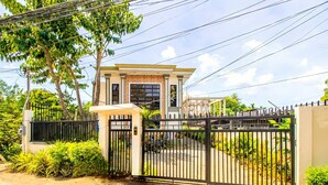 Propiedad residencial privada con reja, una casa de dos plantas, un camino de entrada cubierto y un jardín bien cuidado.