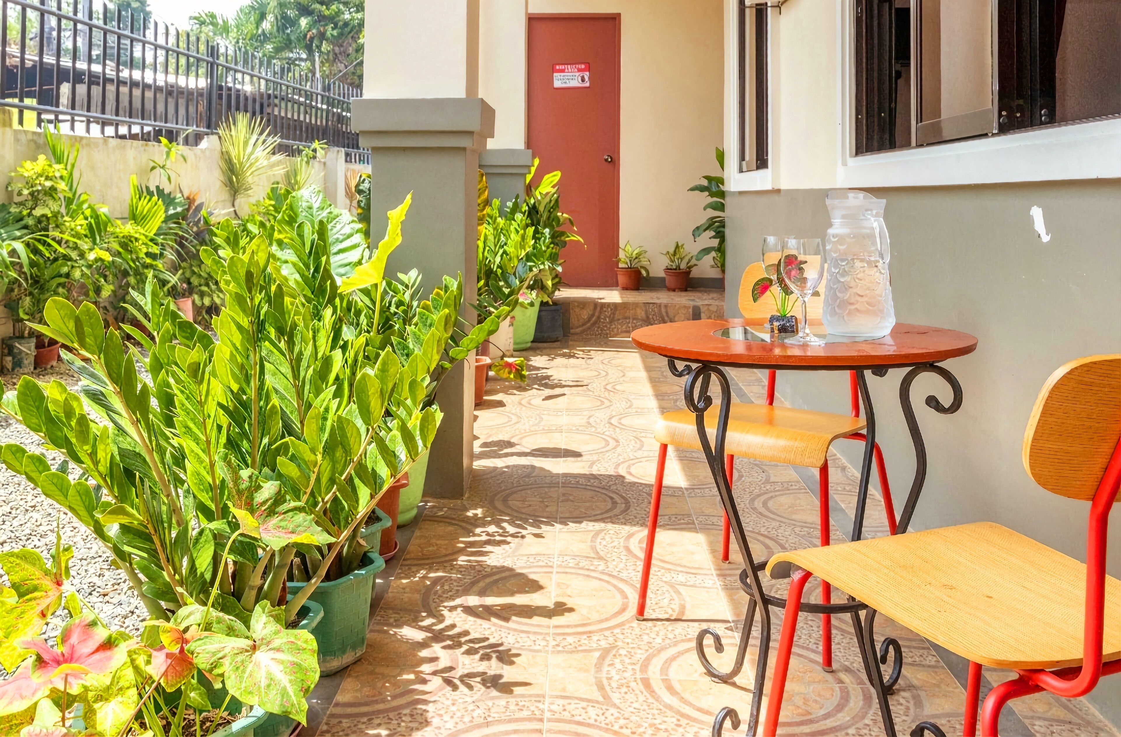 A small outdoor seating area with a table and chairs, surrounded by potted plants.