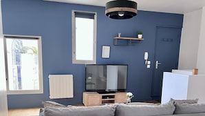 Un salon moderne avec un canapé d’angle gris, une table à manger en bois et un téléviseur posé sur un meuble en bois.