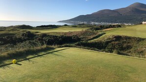 Ein Golfplatz mit Blick auf das Meer und die dahinterliegenden Berge.