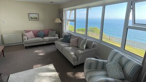 Ein Wohnzimmer mit Meerblick, einer Couch, einem gestreiften Sessel und einer Lampe.