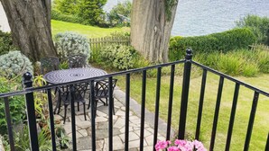 Eine Terrasse mit Tisch und Stühlen, mit Blick auf ein Gewässer und eine Rasenfläche.