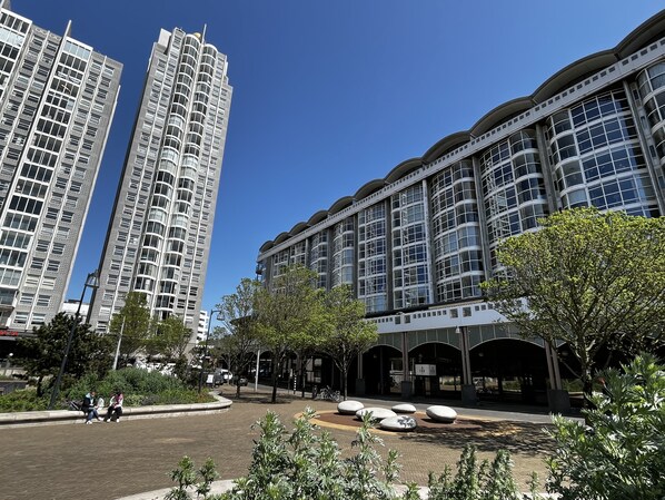 Una zona urbana moderna con edificios altos, una plaza pavimentada con asientos y áreas verdes.