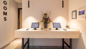 Een receptiebalie met een bordje met daarop 'IN/UIT CHECKEN', twee monitoren, een vaas met bloemen en een ingelijst certificaat aan de muur.