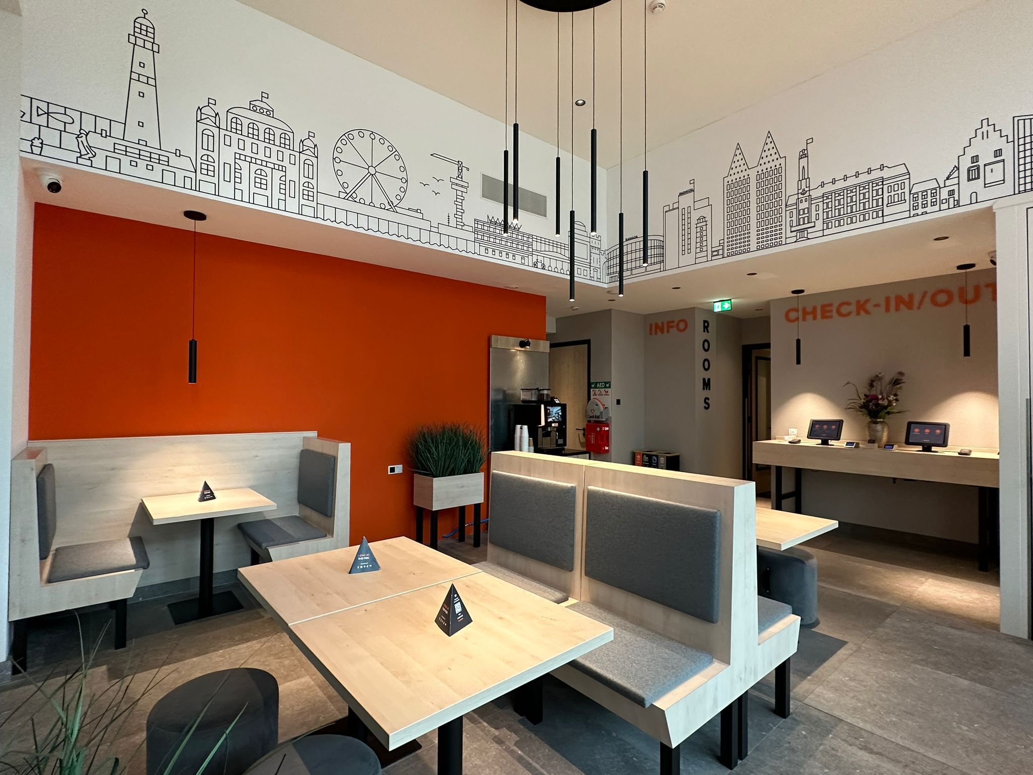 A modern hotel lobby with orange walls, check-in/out counters, and seating areas.