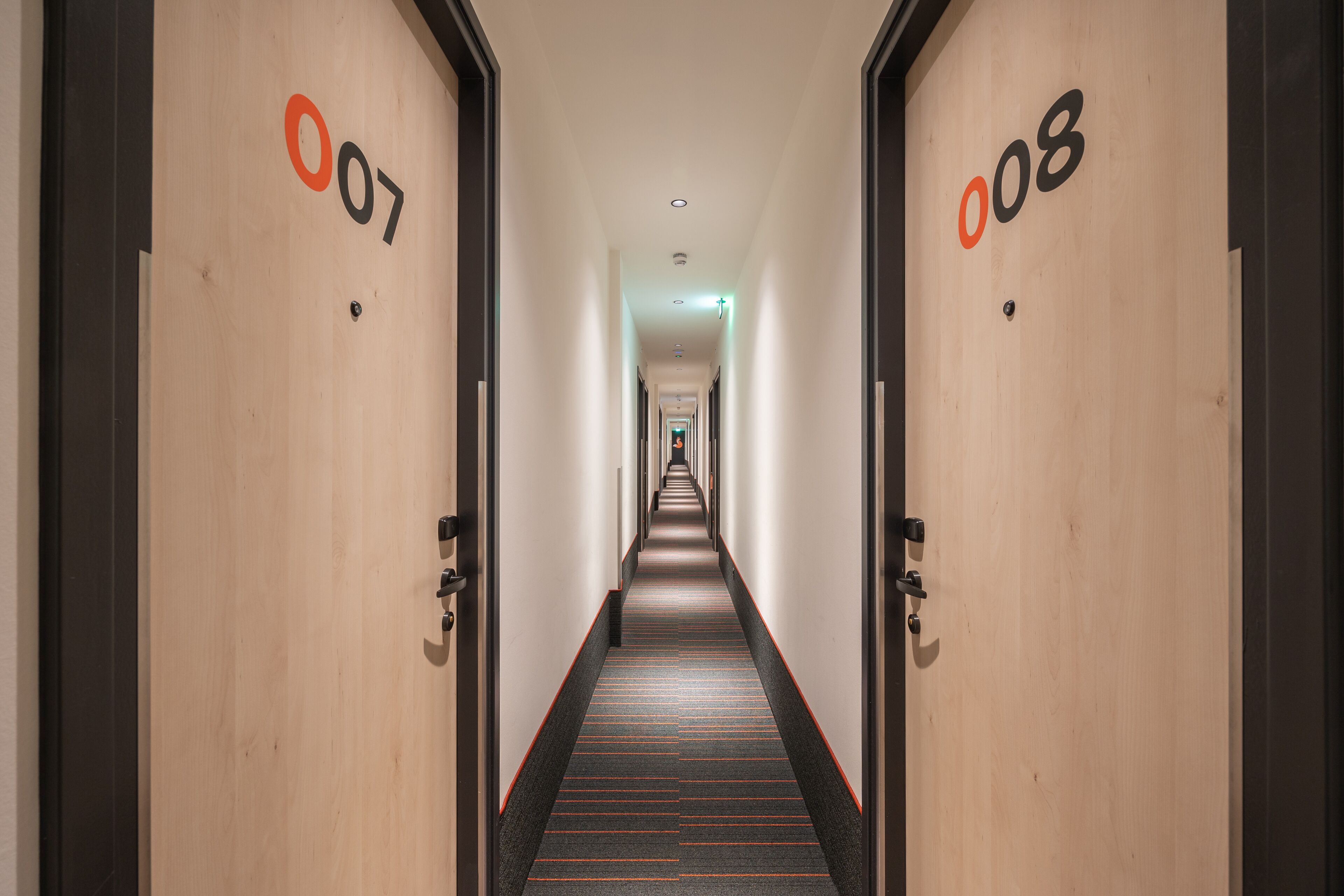 A hotel hallway with doors numbered 007 and 008, leading to a long, straight corridor.