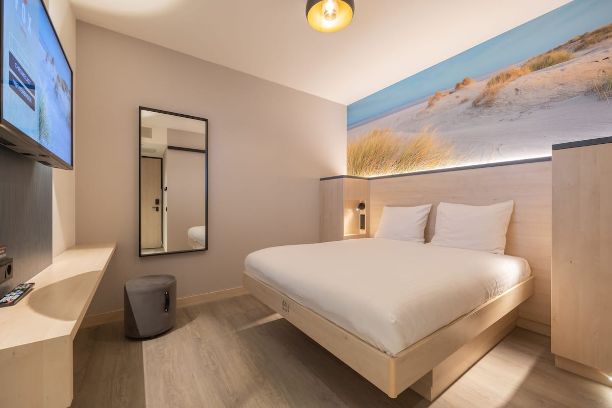 Une chambre à coucher moderne, avec un lit, un téléviseur et un tableau représentant une scène de plage.