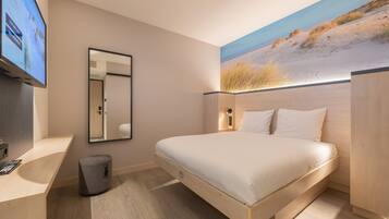 Un dormitorio moderno con una cama, un televisor y un cuadro de una playa.