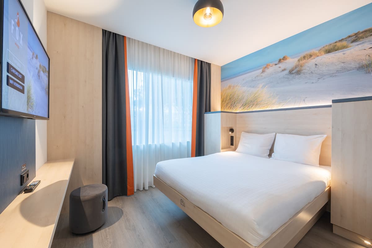 Une chambre d’hôtel moderne avec un grand lit, un bureau et un tableau représentant une scène de plage.