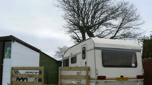 A white RV with a "DRY DOCK" sign, a wooden deck, and a green building in the background.