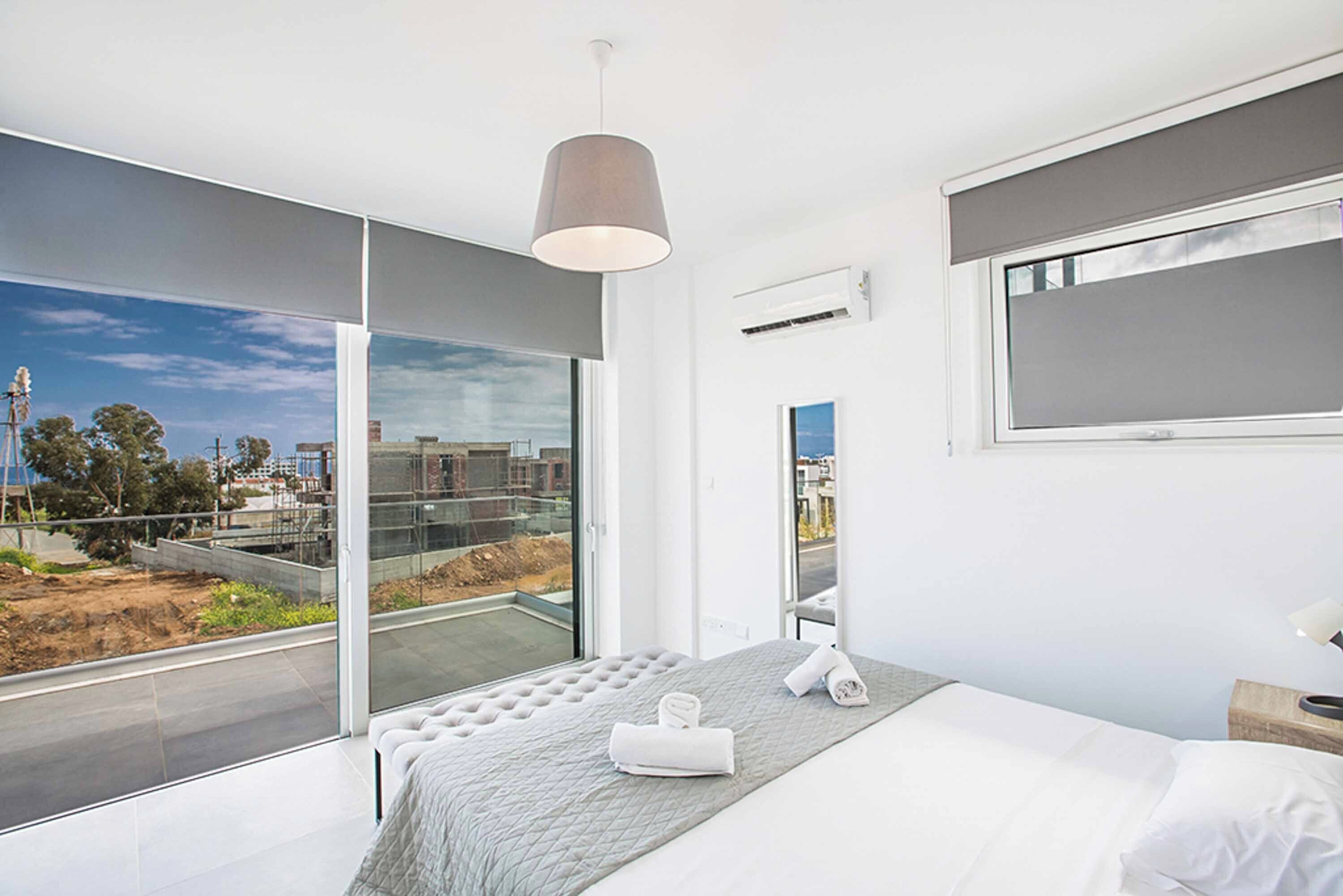 A modern bedroom with a large bed, a view of a construction site, and a hanging light fixture.