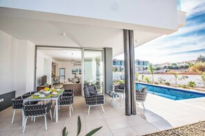 Un'area esterna moderna con zona pranzo e piscina, con una porta vetrata che dà su cucina e soggiorno.