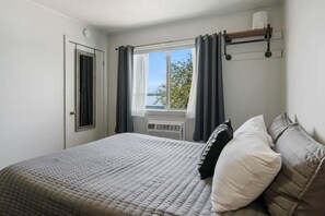 Ein Schlafzimmer mit einem Bett, einem Fenster mit Vorhängen, einem Heizkörper und einem Regal mit einer Tasse.