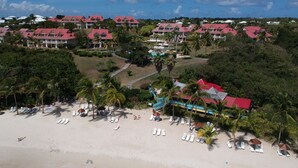 A resort with multiple buildings, a beach with sun loungers, and palm trees. - Appartement vue mer (LE HELLEUX - SAINTE ANNE)
