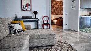 Un salon moderne avec un canapé gris, un fauteuil rouge, un piano et un tableau encadré au mur.
