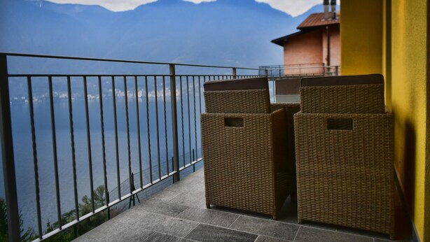 Un balcon doté de meubles en osier, d’une rambarde en métal et offrant une vue sur les montagnes et l’eau.
