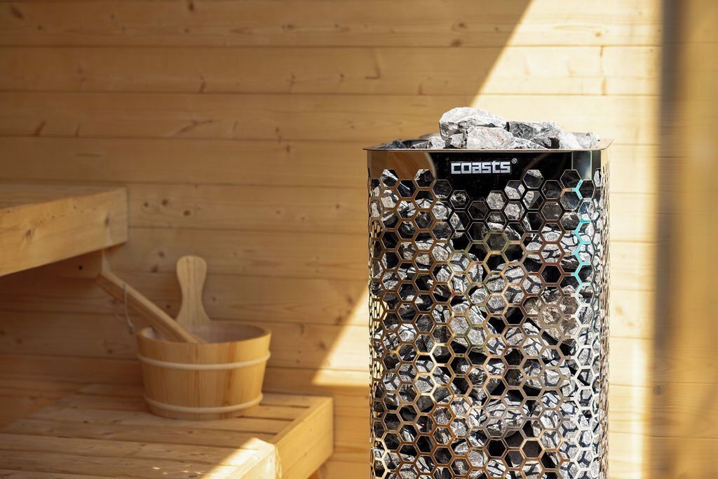 Un sauna doté d’un récipient métallique hexagonal rempli de pierres, d’un banc en bois et d’un seau en bois.