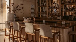 A bar area with wooden bar stools, a counter with bottles, and a wall with framed pictures. - Eastwind Oliverea Valley (Big Indian)